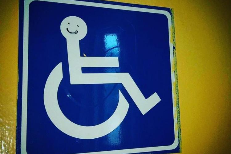 Το λογότυπο των ΑμεΑ, με ένα χαμόγελο ζωγραφιστό στο πρόσωπο του χρήστη του αναπηρικού αμαξίδιου