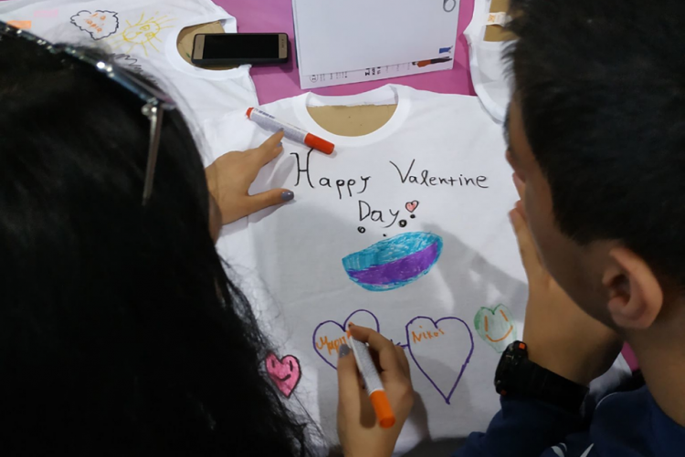 Δύο νέοι, η μία από γενικό και ο άλλος από ειδικό σχολείο, ζωγραφίζουν μαζί ένα μπλουζάκι... μία καρδιά για την Μαργαρίτα, μία άλλη για τον Νίκο και εύχονται έναν χαρούμενο Βαλεντίνο.