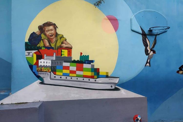 Ο τοίχος του συγκεκριμένου σχολείου ζωγραφισμένος με ένα κορίτσι πάνω σε ένα πλοίο, φτιαγμένο από τουβλάκια LEGOs, και μια μπάλα αφημένη στο πάτωμα.
