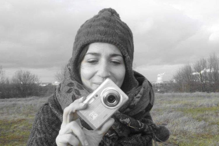 Η Θάλεια με μια φωτογραφική μηχανή χαμογελαστή σε γκρίζο φόντο